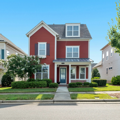 The front of the red house from a street point of view with a sunny, blue sky background.