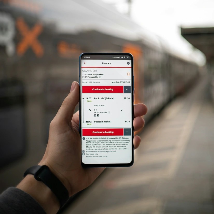 Someone holding a phone up with a train in the background with their boarding information