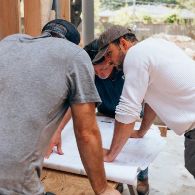 A group of workers all talking over a blueprint outside