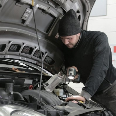 A mechanic working on a car engine under the hood.