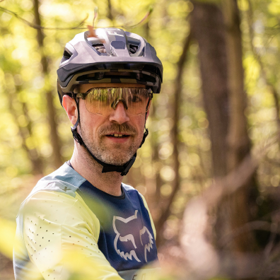 A man in a forest with glasses and a helmet for biking.