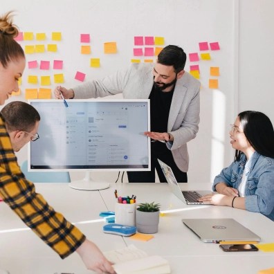 A group of employees at a table all referencing a computer with statistics on the screen.
