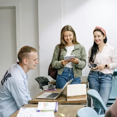 A teacher and two students in a classroom talking at a desk