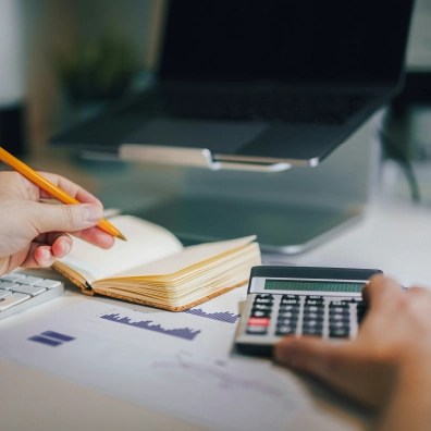 Someone doing calculations with a piece of paper, analytics, and a calculator.