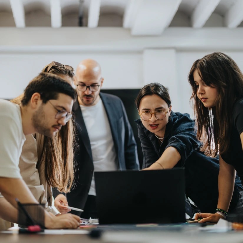 Five coworkers gathered around a laptop collaborating on a project