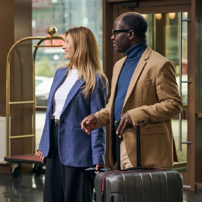 Two hotel guests arriving in a hotel entranceway with luggage