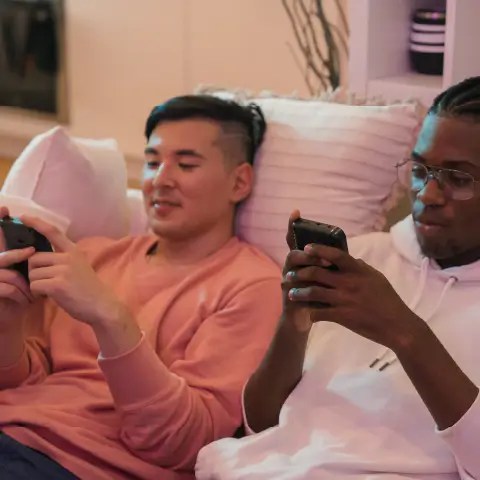 Two men sitting next to each other on a couch starting at their phones