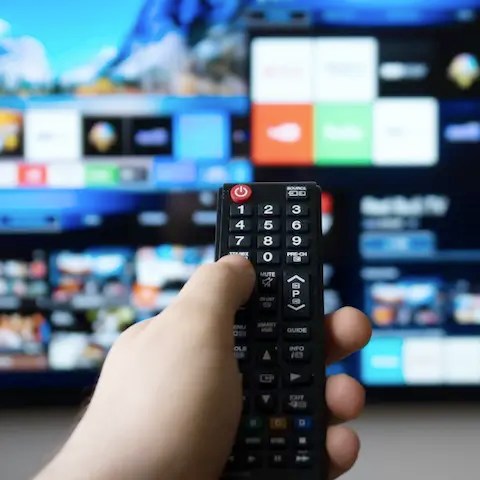 Close up of hand holding a remote in front of a TV