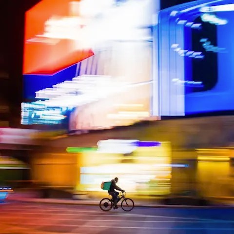 A person biking at night in front of digital out-of-home advertising